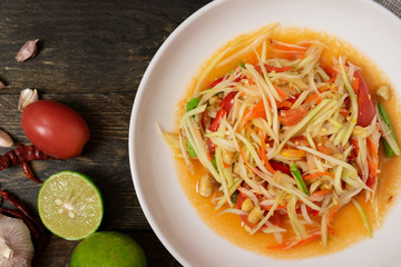 Papaya salad with chili and lemon in white dish on wooden table.(Som Tam Thai)