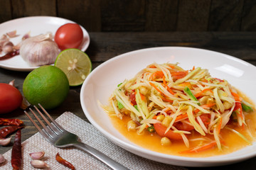 Papaya salad with chili and lemon in white dish on wooden table.(Som Tam Thai)