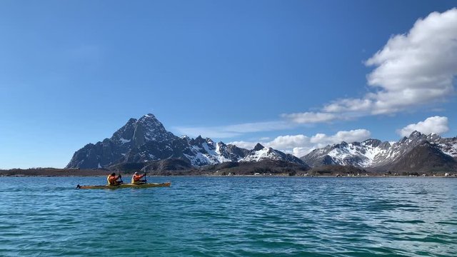 Tandem kayak travelling in front of multiple snow covered mountains in Lofoten, Norway. 