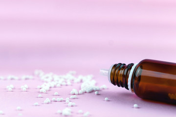 Homeopathic balls and glass bottle on a pink background. Alternative homeopathy herbal medicine, healthcare concept and pills. copyspace for text
