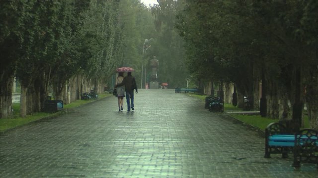Man and a woman are walking under an umbrella in the rain in autumn