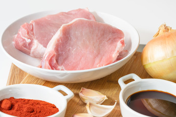 Fresh raw pork meat slices, garlic, onion, soy sauce, and some ingredients on a kitchen table, close up  on white background