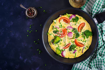 Omelette with broccoli,  tomatoes and red onions in iron skillet. Italian frittata with vegetables. Top view, overhead