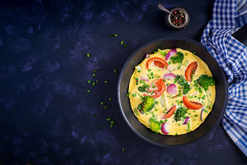 Omelette with broccoli,  tomatoes and red onions in iron skillet. Italian frittata with vegetables. Top view, overhead