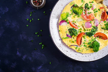 Omelette with broccoli,  tomatoes and red onions on dark table. Italian frittata with vegetables. Top view, overhead