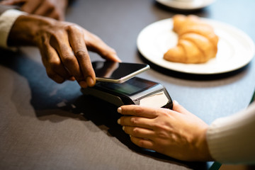 Afro businessman paying with his cellphone at the bar