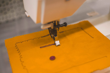 sewing machine sews orange fabric.