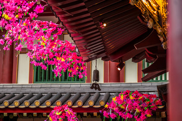 Fototapeta na wymiar Detail of a balcony of a buddist temple in Singapore covered with flowers with a metal bell