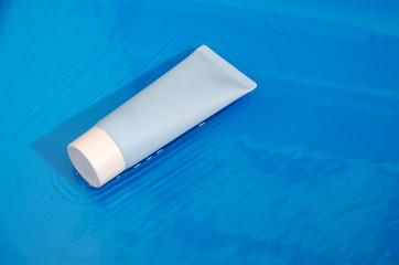 Blue tube with face cream on blue wet background with water waves