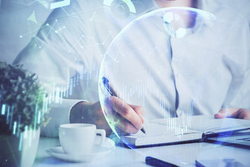 Double exposure of man's hands writing notes of stock market with forex chart.