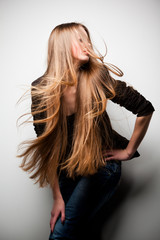 Girl dressed in black jacket, with long flowing hair, posing with her head turned to side against white wall