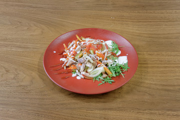 Restaurant food served on a red plate. Fish, cheese, salad, vegetables, sauce.
