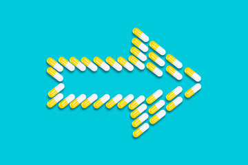 Yellow pills in the shape of an arrow on a blue background. Medicine, pills background. Treatment.