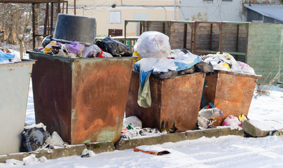 Rusty dumpsters open. Trash is scattered around containers. Environmental pollution