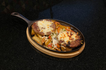 Grilled meat served in a pan on a black background.