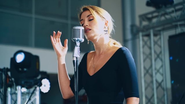 Musical star on the stage. Attractive woman singer performing a live music into the microphone for special event. Slow motion.