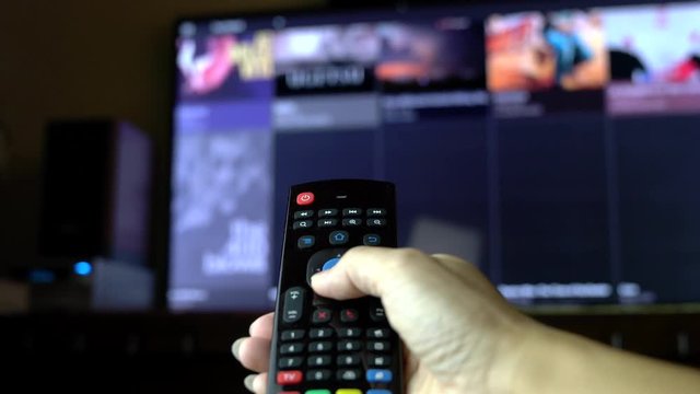 Hands holding tv remote control to select tv programs on smart tv. Movie selection surfing, focus on hand and remote control. Internet tv concept.