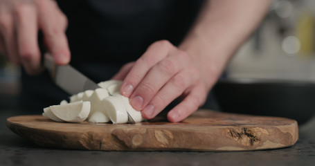 man slicing fresh mozzarella cheese on olive wood board