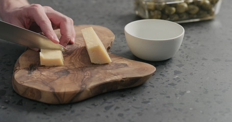 man slicing parmesan cheese on olive wood board