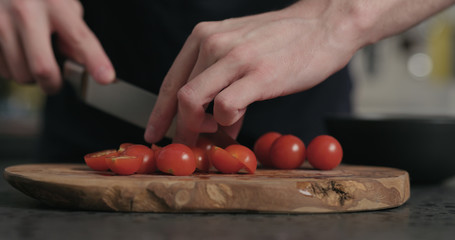 man cut cherry tomatoes on olive wood board