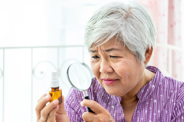 Senior elder woman female looking at and checking medicine container with magnifying glass