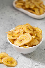 Dried bananas in a white ceramic bowl on a gray kitchen table. Banana chips. Vegetarian snack for proper nutrition	