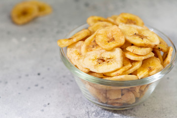 Dried bananas in a glass bowl on a gray kitchen table. Banana chips. Vegetarian snack for proper nutrition
