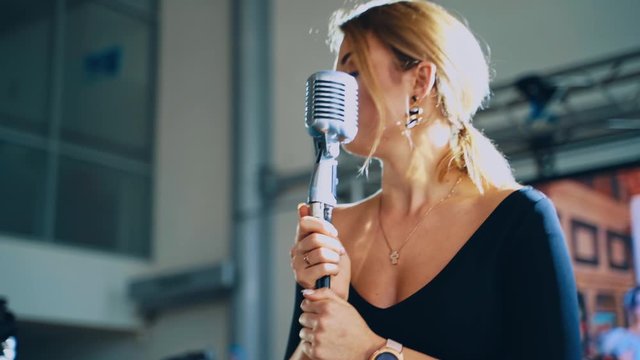 Attractive woman singing into a mic. Professional singer standing at the microphone and performing a live music. Slow motion.