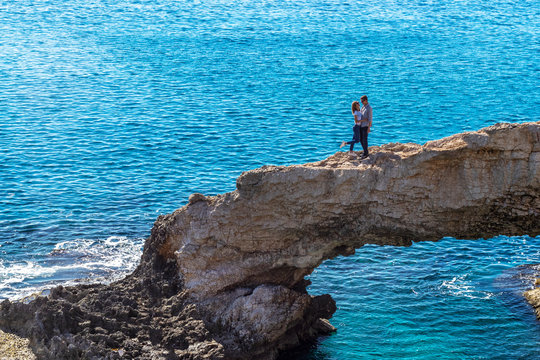 Couple in love are hugging on the natural stone bridge on blue sea background.
