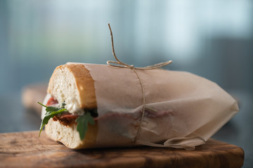 Ciabatta sandwich with salame, arugula, red pesto and cream cheese wrapped in paper on olive board