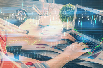 Double exposure of stock graph with businessman typing on computer in office on background. Concept of hard work.