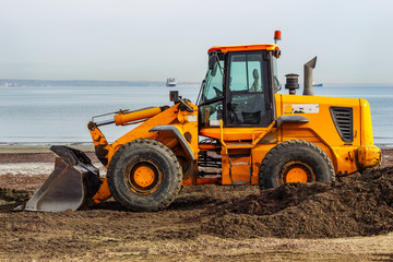 Yellow grader leveled the land by the sea. The process of preparing the beach for the summer season.
