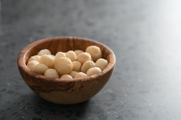 Macadamia nuts in olive wood bowl on terrazzo surface with copy space