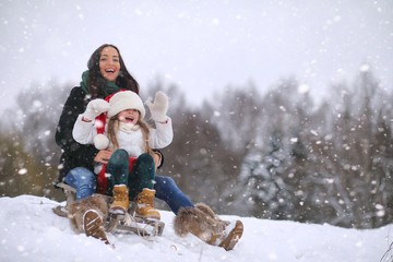Obraz premium A winter fairy tale, a young mother and her daughter. A girl on a sled with gifts on the eve of the new year in the park. Two sisters walk in a New Year's park and ride a sled with gifts.