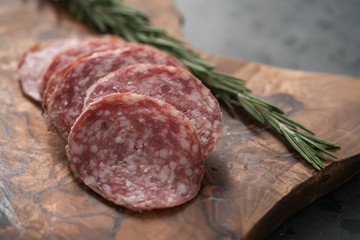 Sliced salame milano sausage on olive wood board with rosemary