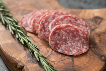 Sliced salame milano sausage on olive wood board with rosemary