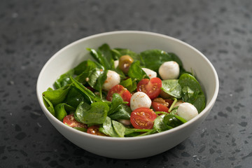 Salad with cherry tomatoes, spinach leaves and mozzarella balls in white bowl on terrazzo surface