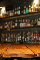 Wooden board on a background of bottles with alcohol. Old bar counter as layout for design. Workpiece for design. Empty place to advertise products. Blurred interior of the bar in the background.