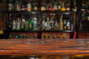 Wooden board on a background of bottles with alcohol. Old bar counter as layout for design. Workpiece for design. Empty place to advertise products. Blurred interior of the bar in the background.