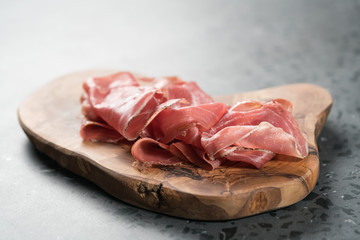 Sliced prosciutto ham on olive wood board