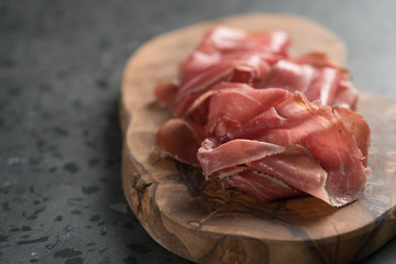 Sliced prosciutto ham on olive wood board