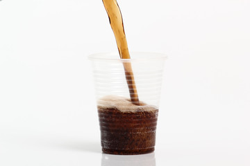 Pouring cola into plastic cup. Isolated on white background.