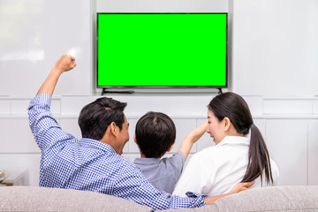 Back view of happy Asian family watching TV together in living room at home; cheerful and fun with movie, with green screen