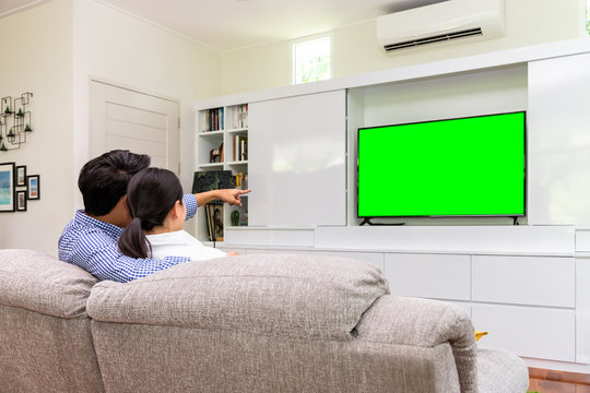 Back View Of Asian Couple Sitting On Sofa Relaxing And Enjoy Watching TV At Home With Green Screen