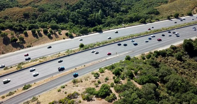 Aerial bird's eye view of light afternoon traffic on California highway with trees and foliage on both sides