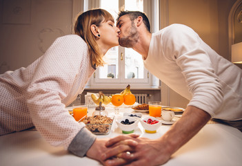 Obraz na płótnie Canvas Good morning! Beautiful couple in love kiss and have breakfast at home eating and drinking healthy food.