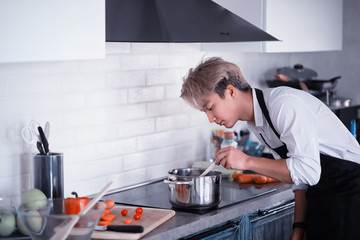 Asian cook in the kitchen prepares food in a cook suit