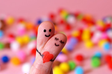 Naklejka premium valentine's day, Happy couple in love. 2 fingers holding red heart while smiling face with multicolored bokeh background. happy couple in love with painted smiley and hugging. colorful spots