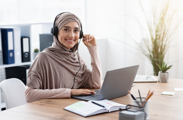 Arabic female employee in headset watching webinar on laptop in office