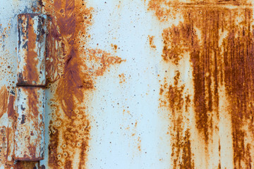 Detail of a rusty door on rusty hinges.Rust background with scratches and remnants of blue paint.